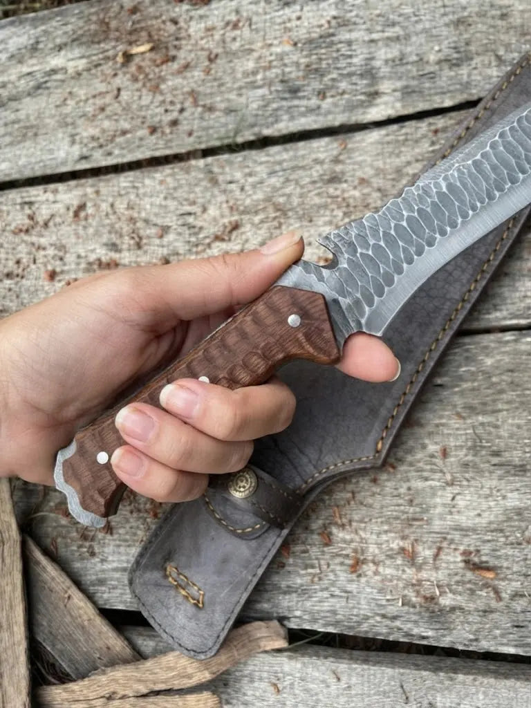 Hand-held view of a custom textured hunting knife with a wooden handle and matching leather sheath