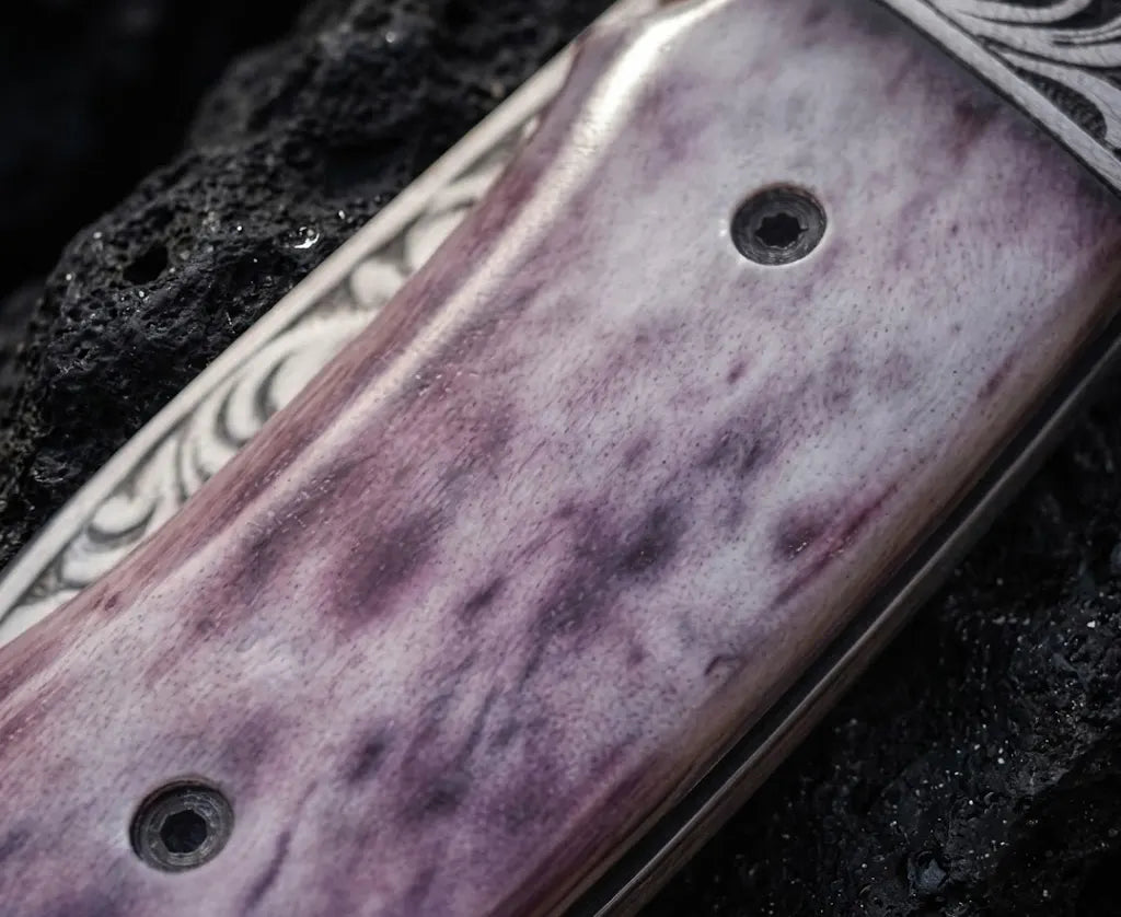 Macro close-up shot of a smooth purple-stained natural bone handle scale with torx pin fasteners on a custom handmade folding pocket knife.
